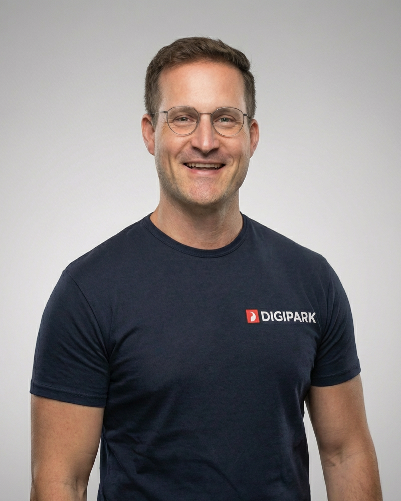 Heiko Bucher, DIGIPARK Gründer und Geschäftsführer. Ein Mann mit braunen Haaren, blauem T-Shirt mit DIGIPARK-Logo auf der Brust, vor grauem Hintergrund.