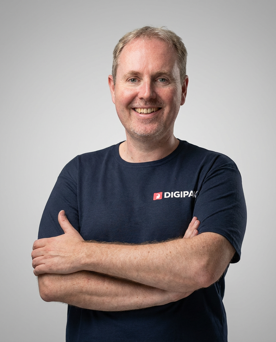 Michael Huttny, DIGIPARK Gründer und Geschäftsführer. Ein Mann mit blonden Haaren, blauem T-Shirt mit DIGIPARK-Logo auf der Brust, verschränkten Armen vor grauem Hintergrund.