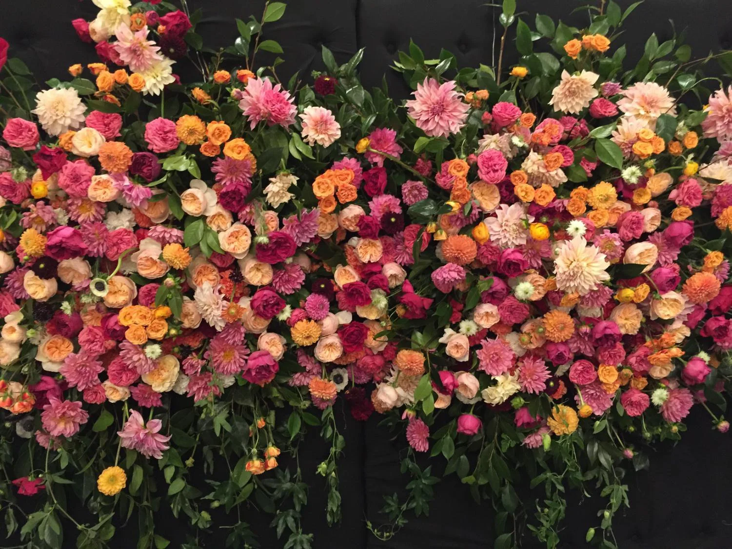 A colorful arrangement of pink, orange, yellow, white, and dark red flowers with green leaves against a dark background.