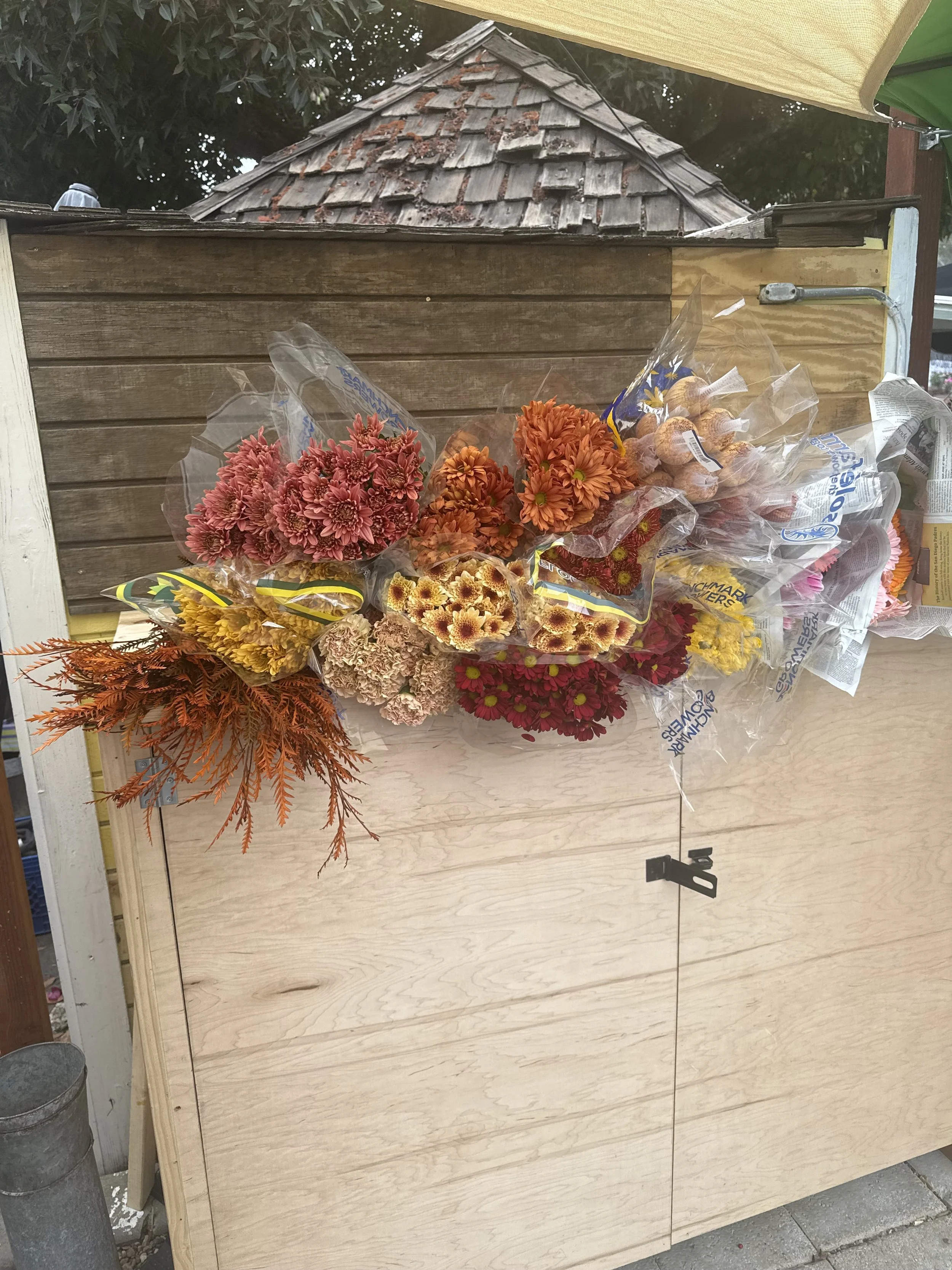 Bundles of colorful artificial flowers resting on top of a wooden box outside.