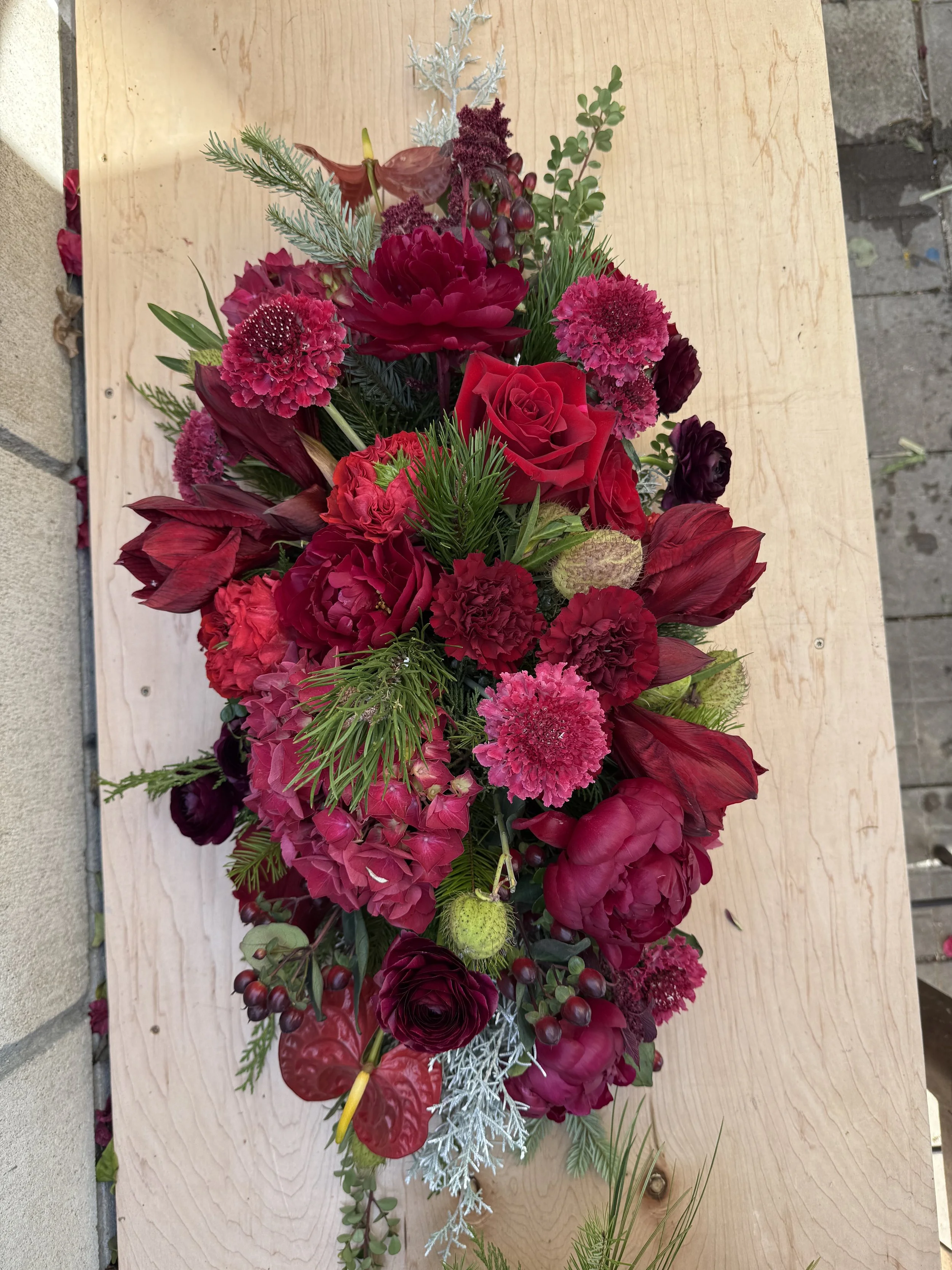 A colorful floral arrangement of various red, pink, and purple flowers on a wooden surface.