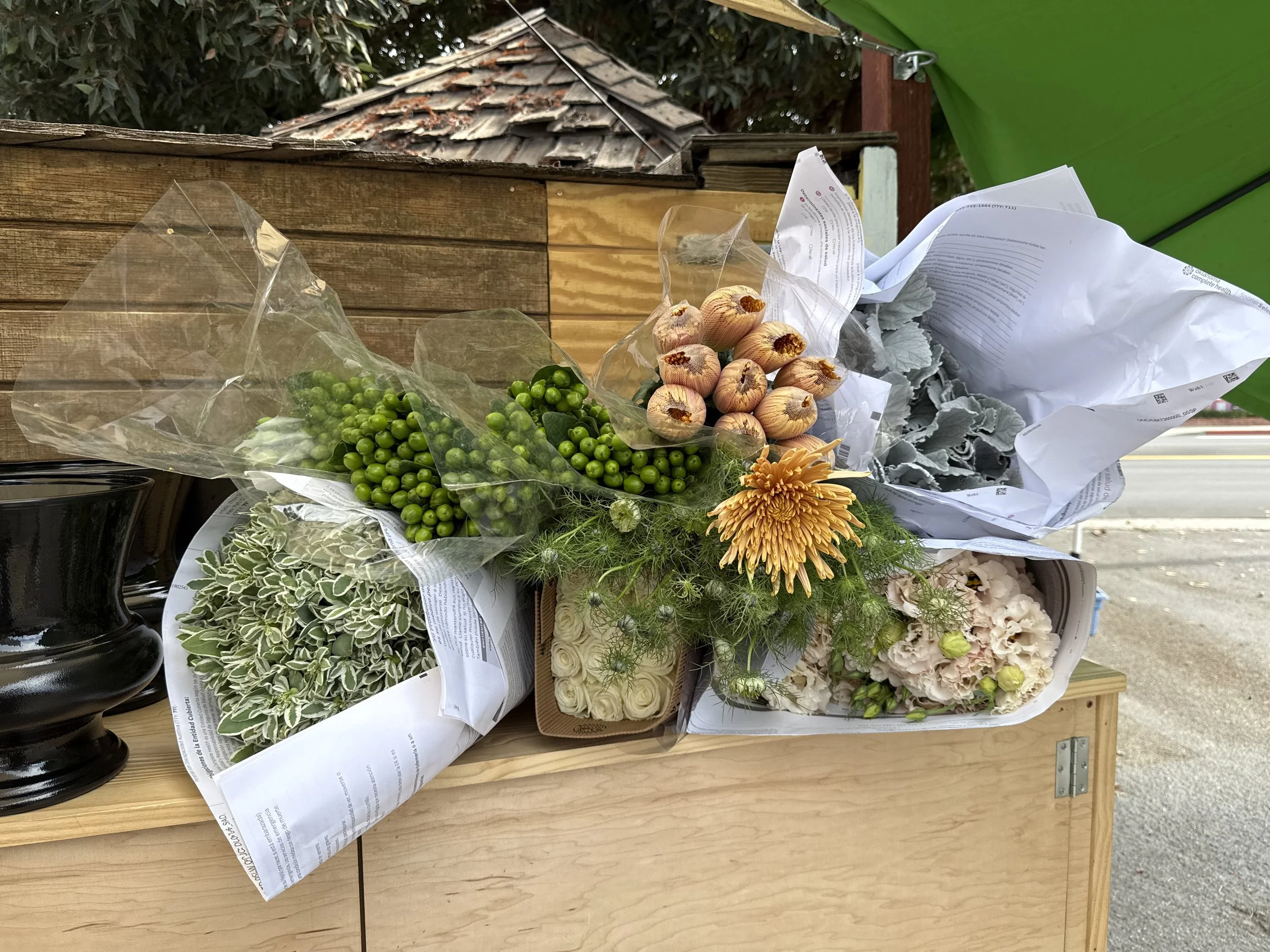 Bouquets of flowers and a bunch of garlic on a wooden table outside.