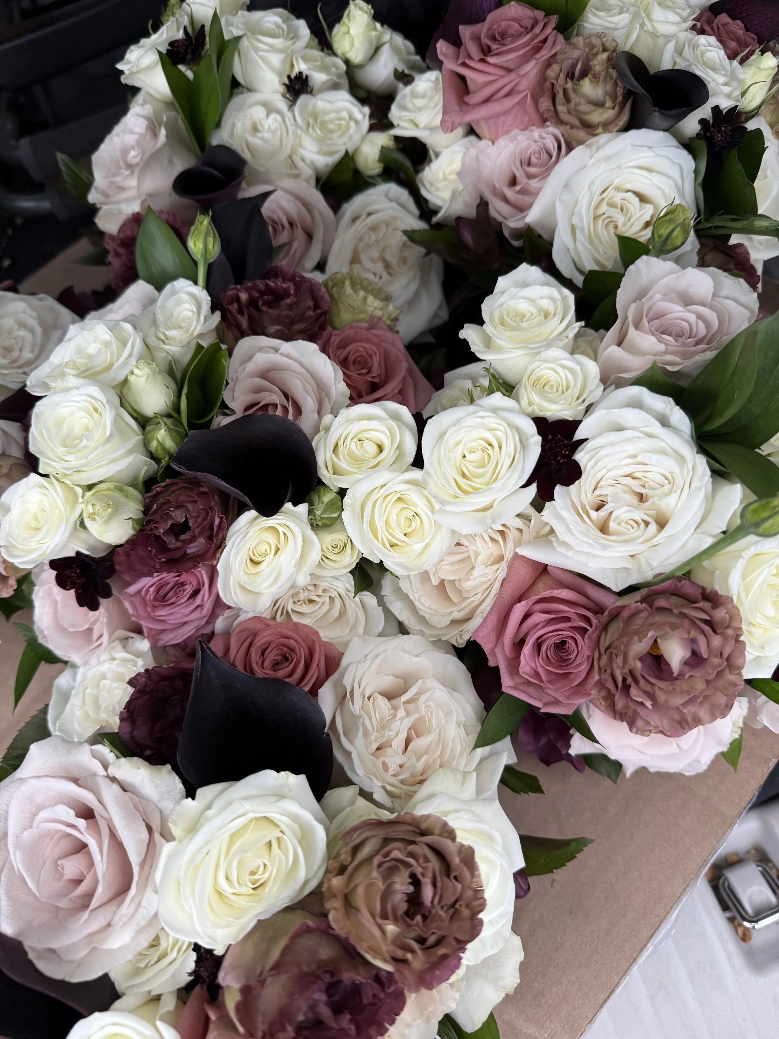 A large bouquet of flowers with pink, white, and purple roses, along with dark purple calla lilies and green leaves.