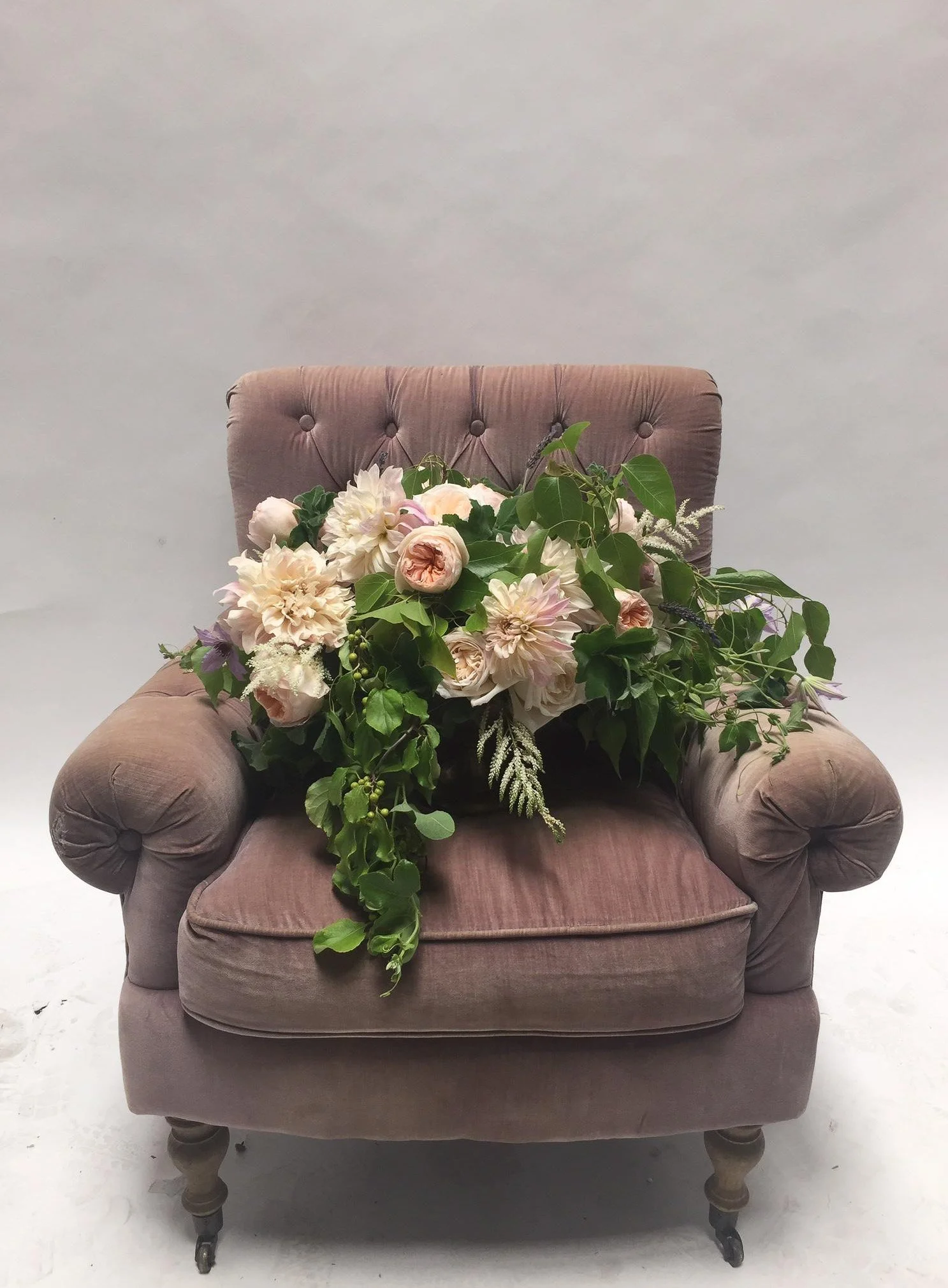 A vintage pink upholstered armchair with a floral arrangement of pink and white flowers and green foliage on the seat.