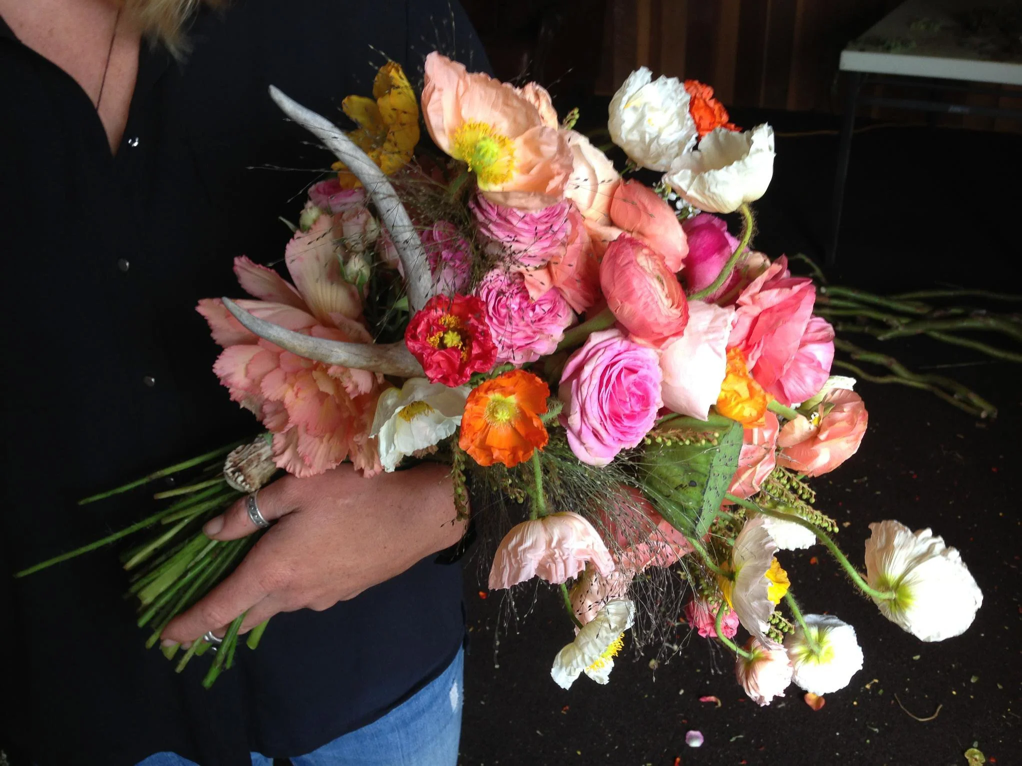 Person holding a large colorful flower bouquet with pink, white, orange, and yellow flowers, and green leaves.