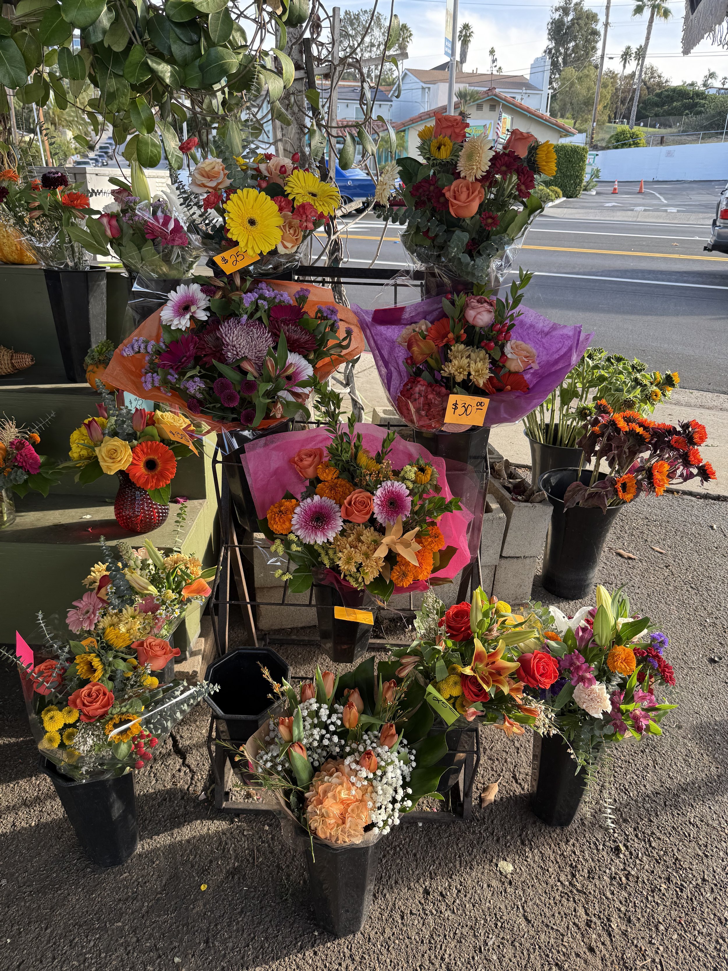 Various colorful flower bouquets displayed outside a shop on a sidewalk, with hand-written price tags.