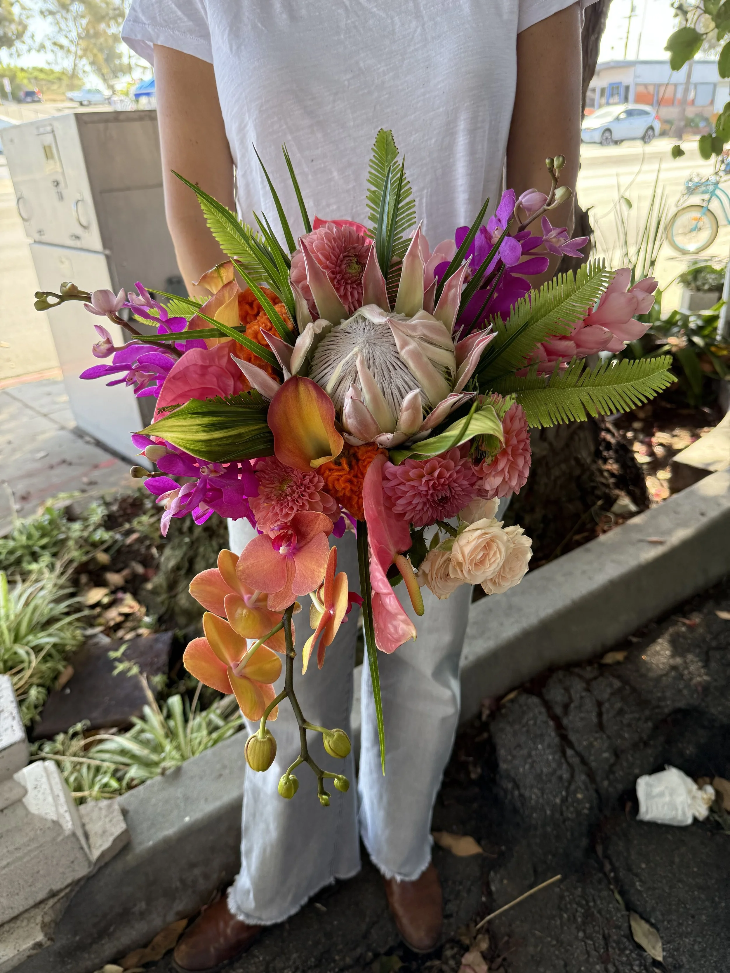 Person holding a vibrant bouquet of various colorful flowers including orchids, roses, and tropical blooms.