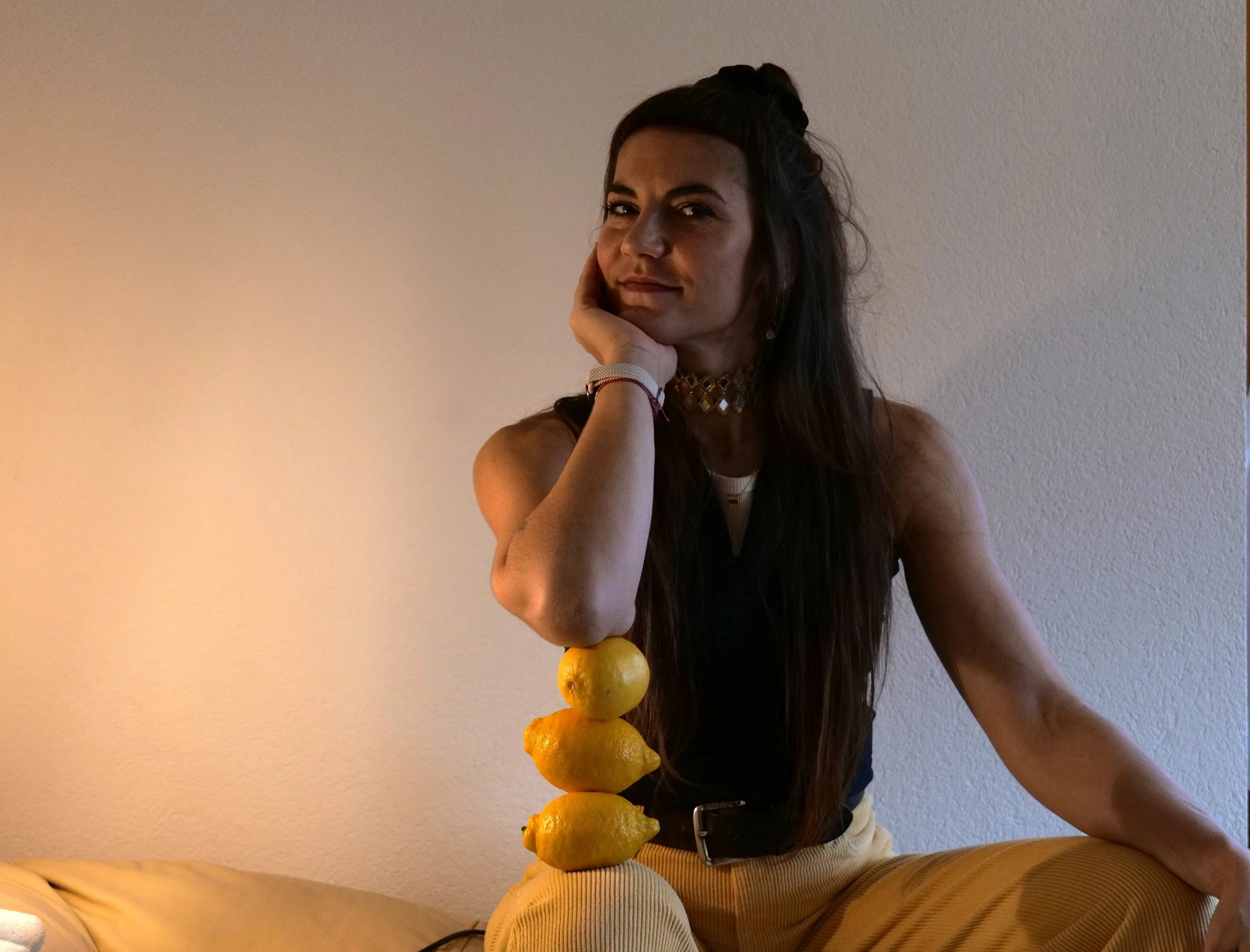 Junge Frau sitzt auf dem Boden, ruht den Kopf auf ihrer Hand, neben ihr gestapelte Zitronen und Limonen.