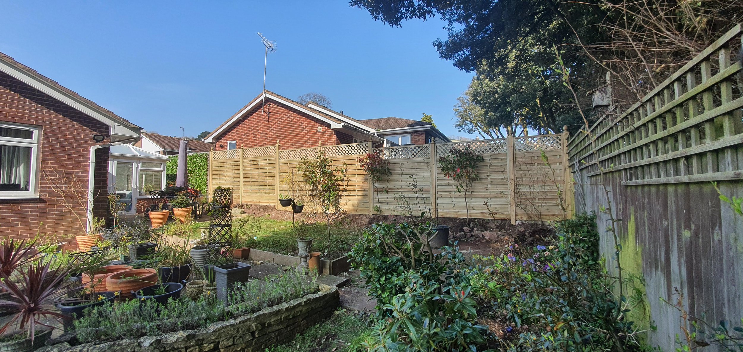 Backyard garden with potted plants, small trees, and a lawn, enclosed by a wooden fence.