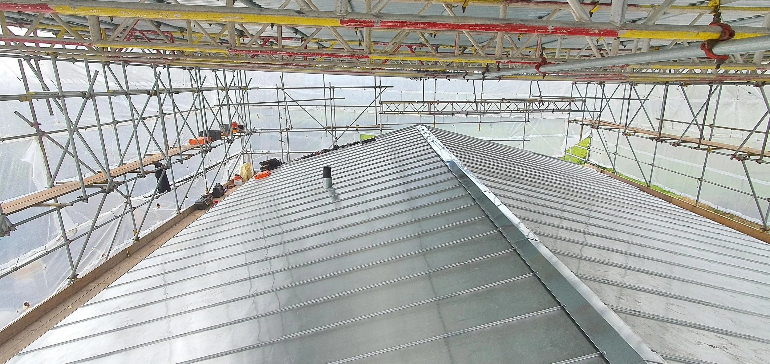 Construction scaffolding surrounds a building's roof, which is being repaired or replaced with metal panels.