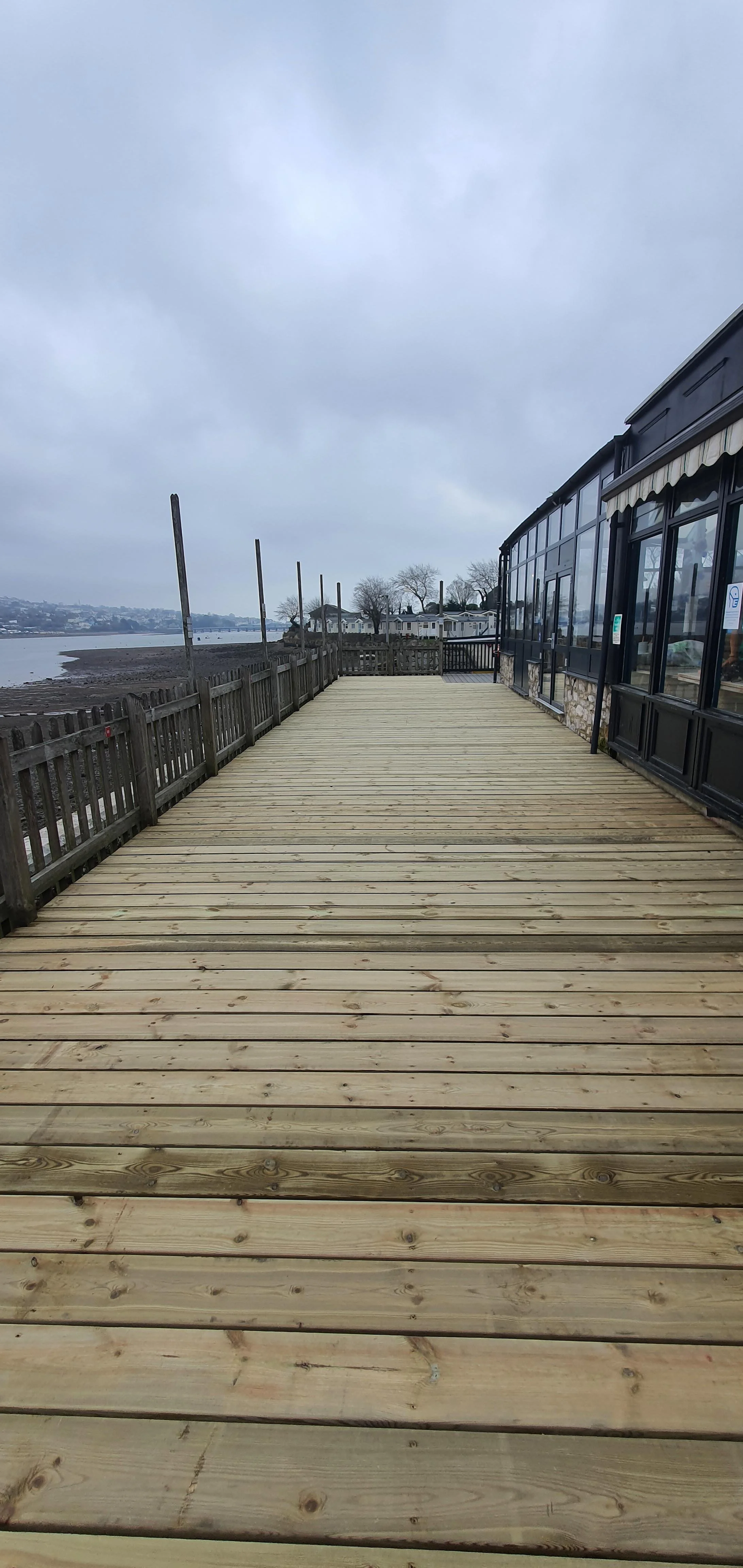 Empty wooden deck with a view of the water and overcast sky.