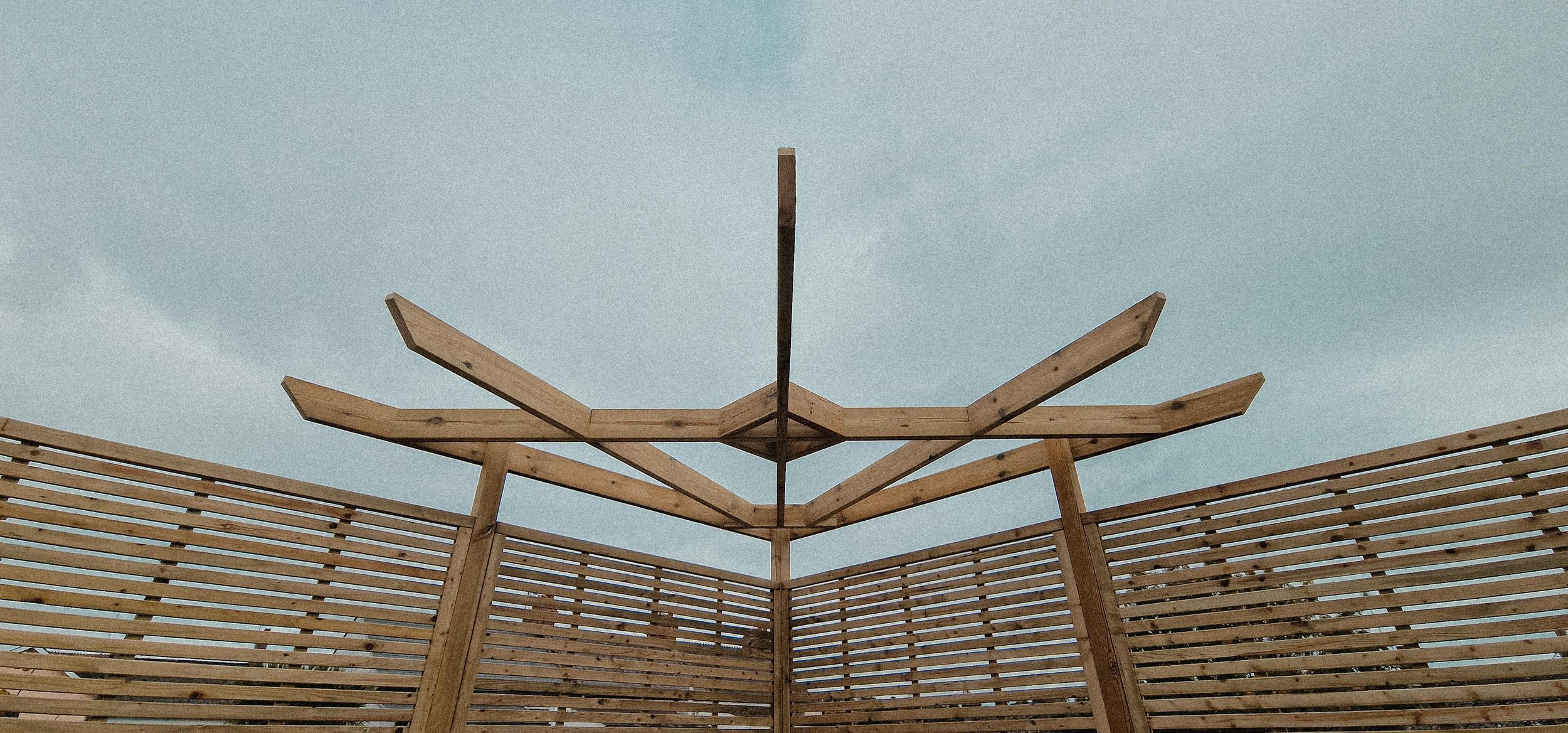Partially constructed wooden pergola with slatted walls against a cloudy sky