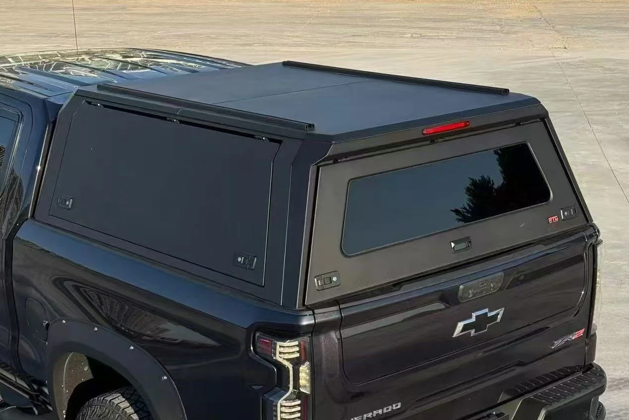 Black Chevrolet Silverado pickup truck with a matching black camper shell on the bed, parked on a concrete surface.