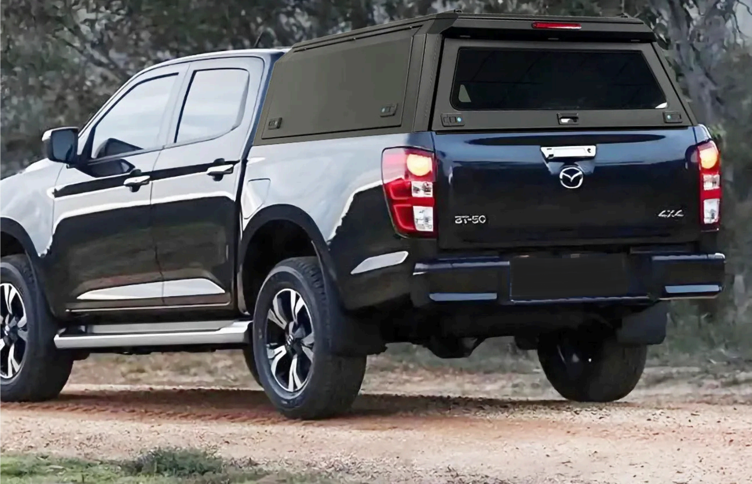 Black and white pickup truck with a black bed cap, driving on a dirt road in a rural area.