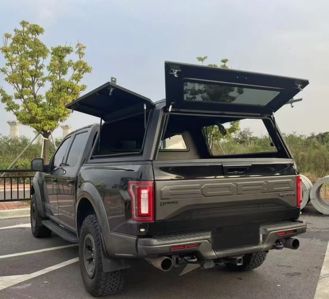 A black Ford F-150 pickup truck with the tailgate and canopy open in a parking lot, with trees in the background.