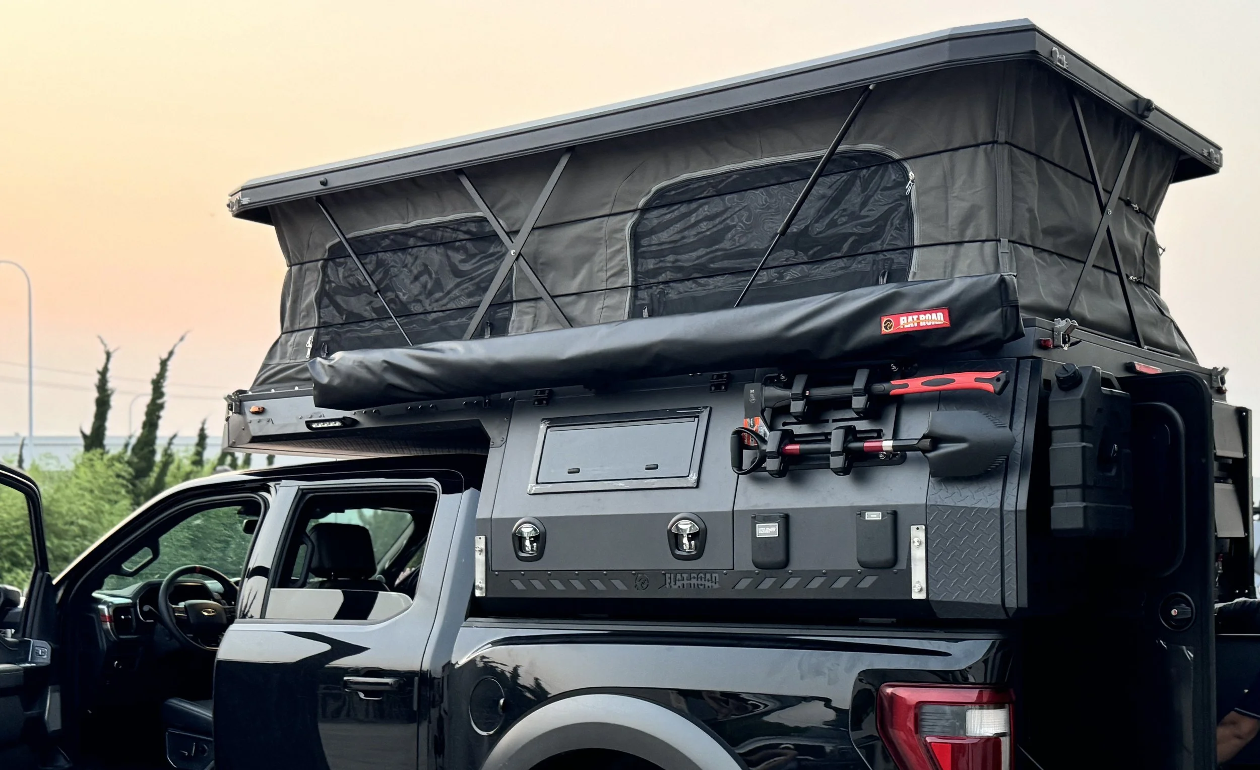 A black pickup truck equipped with a rooftop tent, tools, and storage compartments for outdoor camping.