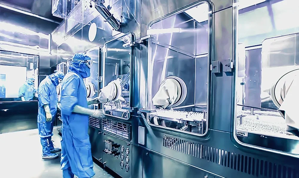 Laboratory workers in blue protective suits and masks working with high-tech equipment in a sterile, metallic environment.