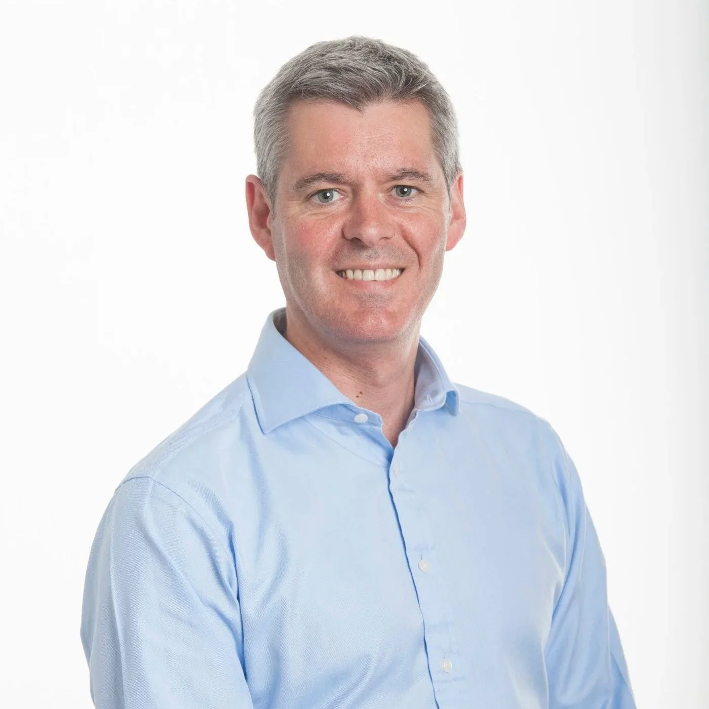 David is wearing a blue shirt and has silver hair, blue eyes and an attractive smile.