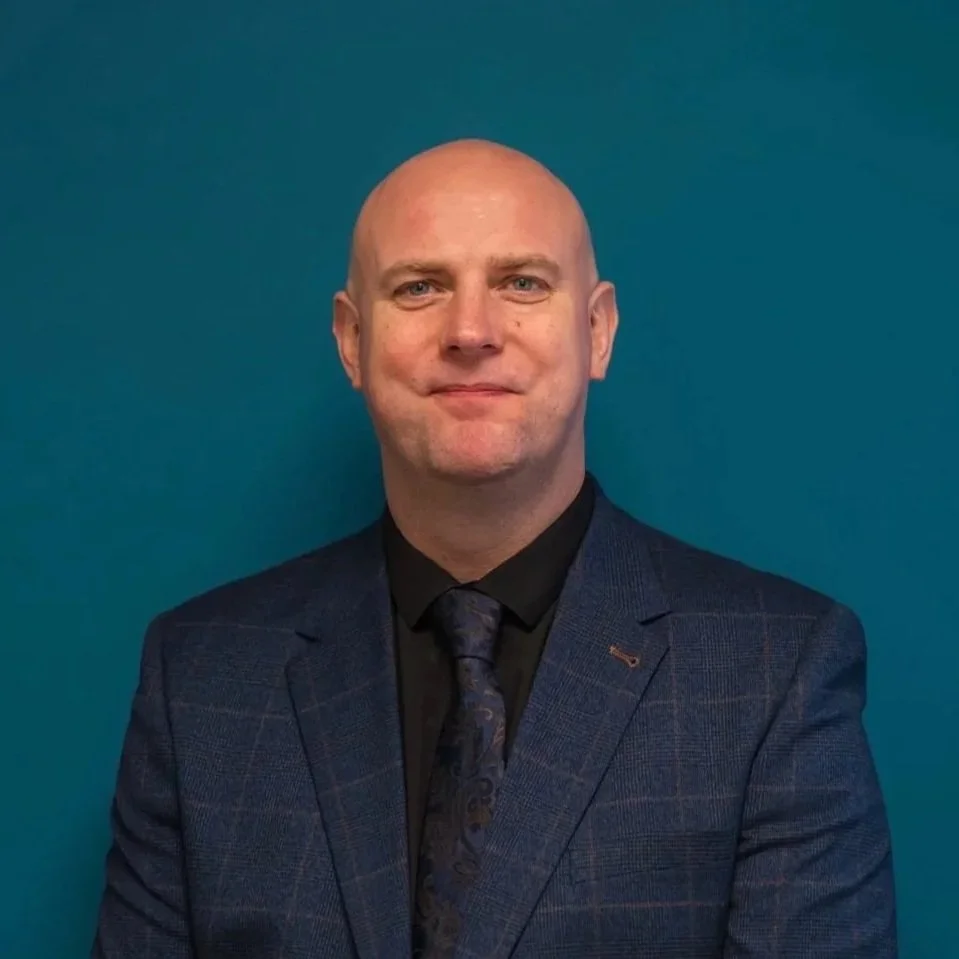 Kurt is known for being balk, he has blue eyes and is smiling at the camera, with a dark suit, shirt and tie.