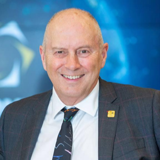 Neil Longfellow looking at the camera and smiling, not a lot of hair, wearing a smart suit, shirt and tie. 