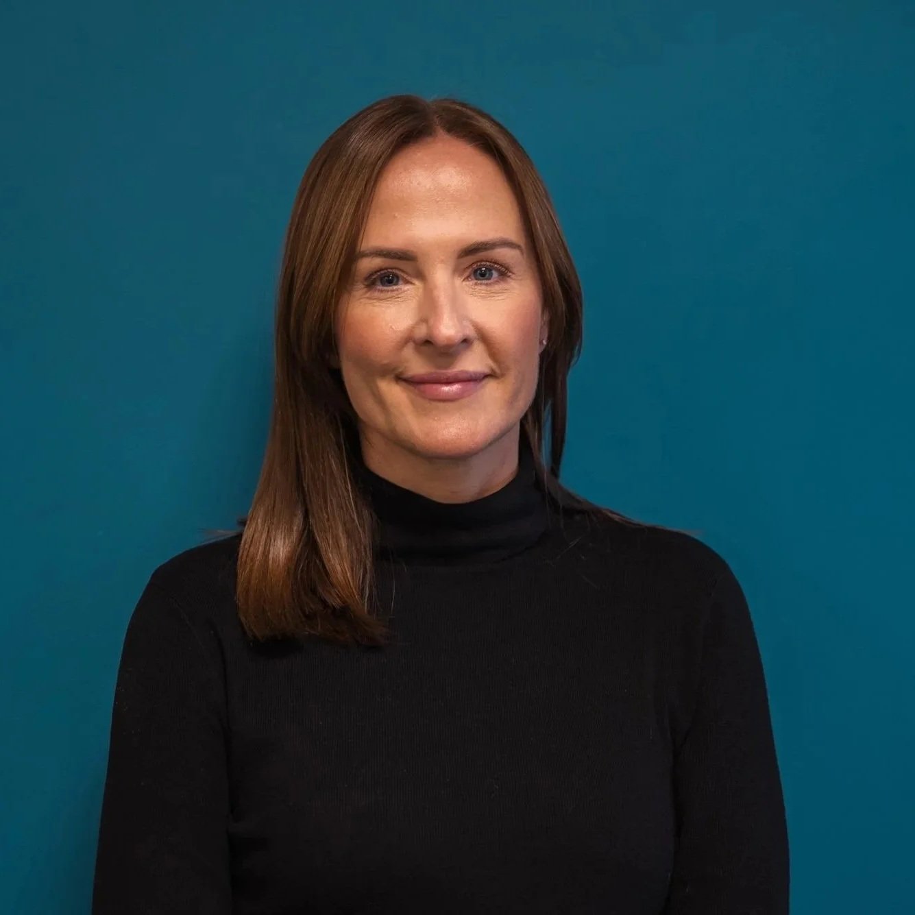 Amy is wearing a polo neck and has shoulder length brown hair, she has a friendly smile.