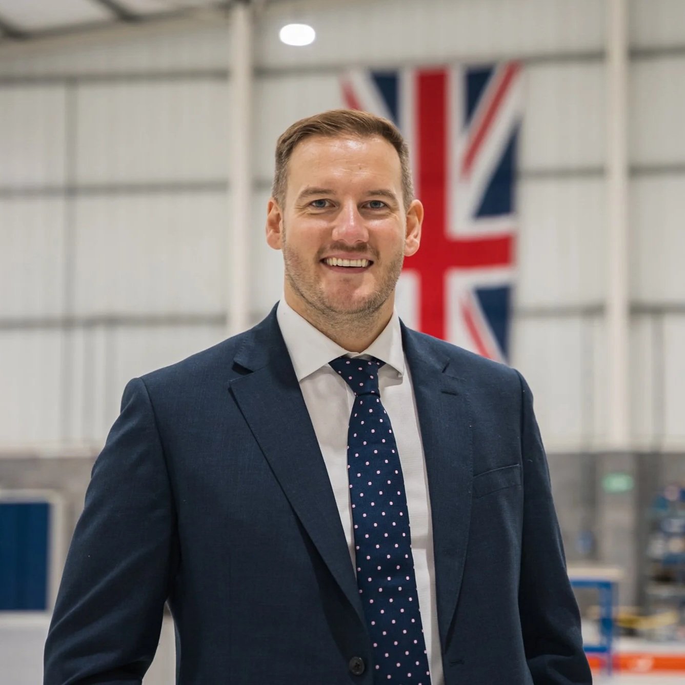 Stephen has a smart blue suit, white shirt and blue polka dot tie. He has a very friendly smile and a union flag is on the wall  behind him in Delkia's production facility in Haydock. 