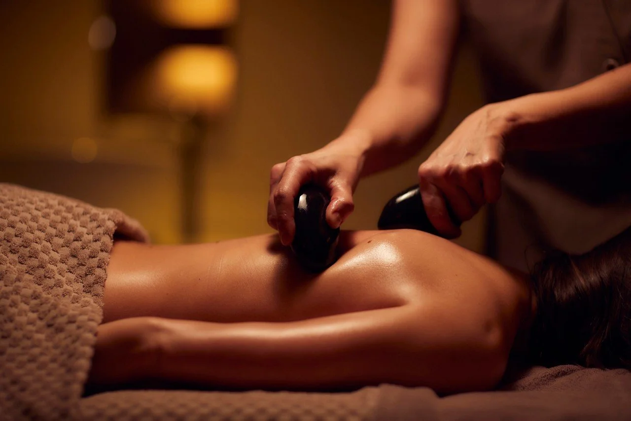 A person receiving a hot stone massage on their back in a spa setting.