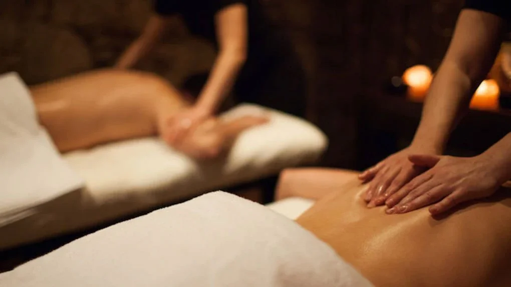 Two people receiving massages in a dimly lit spa room with candles.