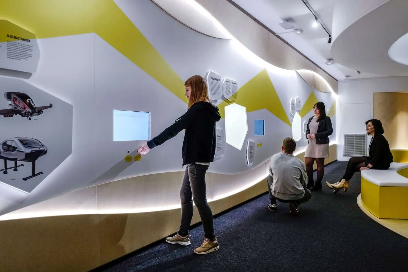 Groupes de personnes dans un musée ou une exposition avec des affichages interactifs et des vidéos.