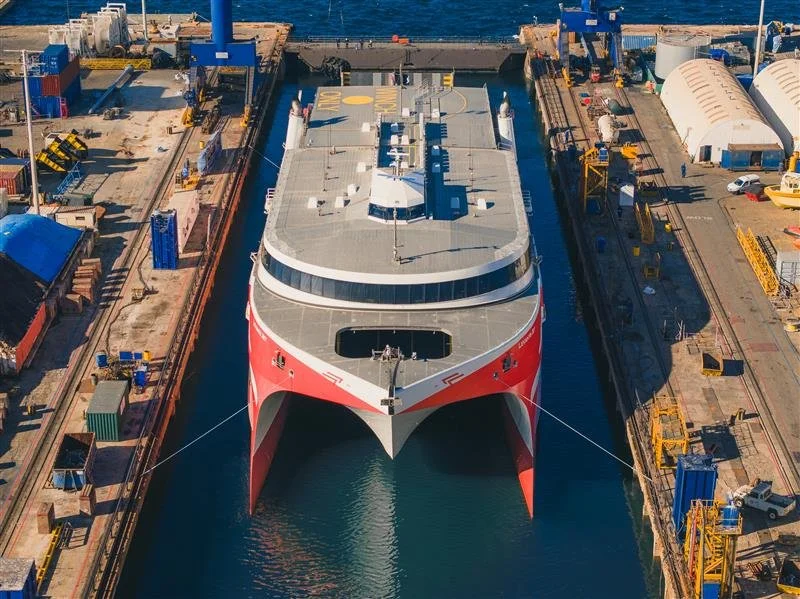 A large cruise ship docked in a shipyard with industrial equipment surrounding it.