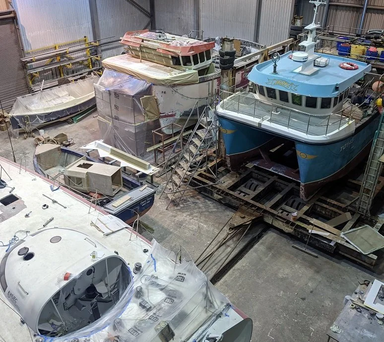 Indoor boat workshop with multiple boats in various stages of construction and repair.