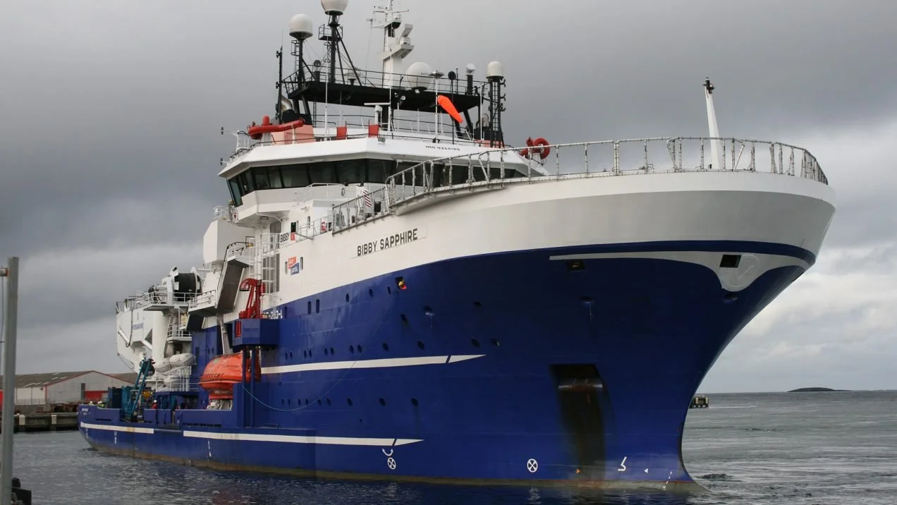 Large ship named Bibby Sapphire docked at a harbor, with a dark, cloudy sky in the background.