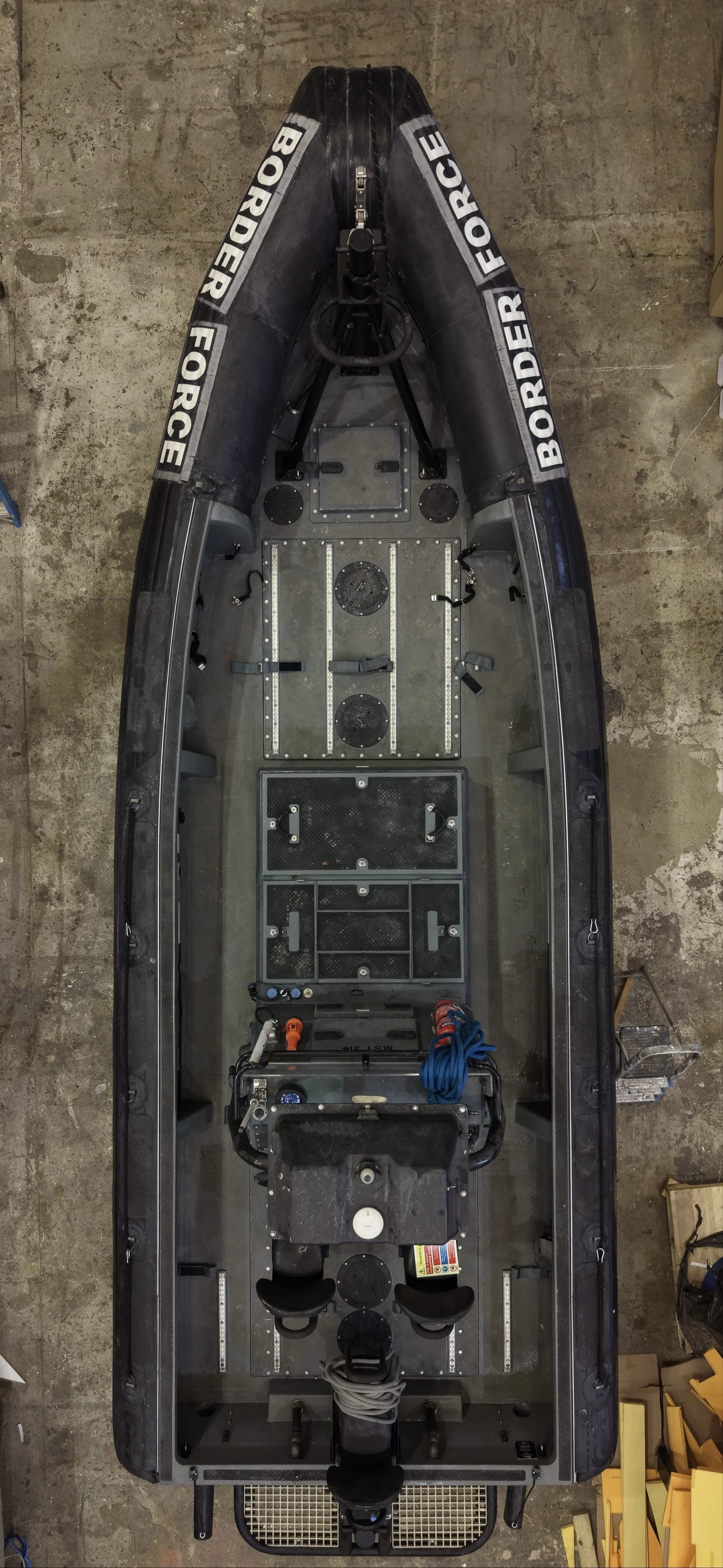 Top view of an empty black boat with branding 'Border Force' on the sides, showing the interior structure, seating, and equipment compartments.