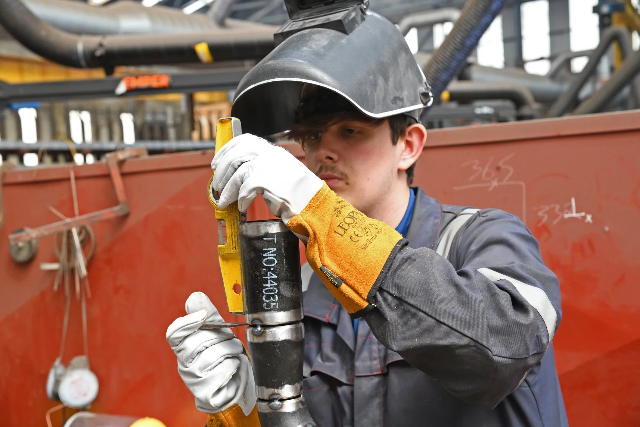 A Balaena technician wearing safety gloves and a helmet working with a large hydraulic jack in an industrial setting. The background shows equipment and machinery.