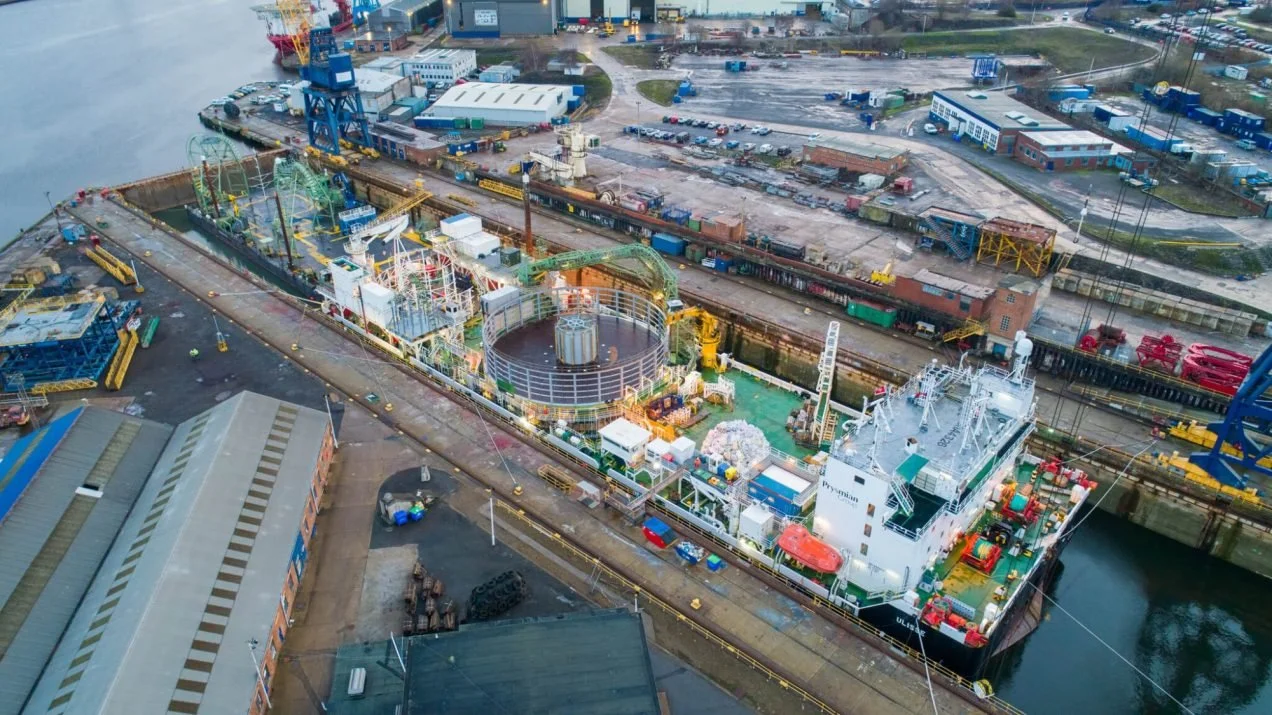 Large ship in a shipyard being built inside a factory with cranes and scaffolding.