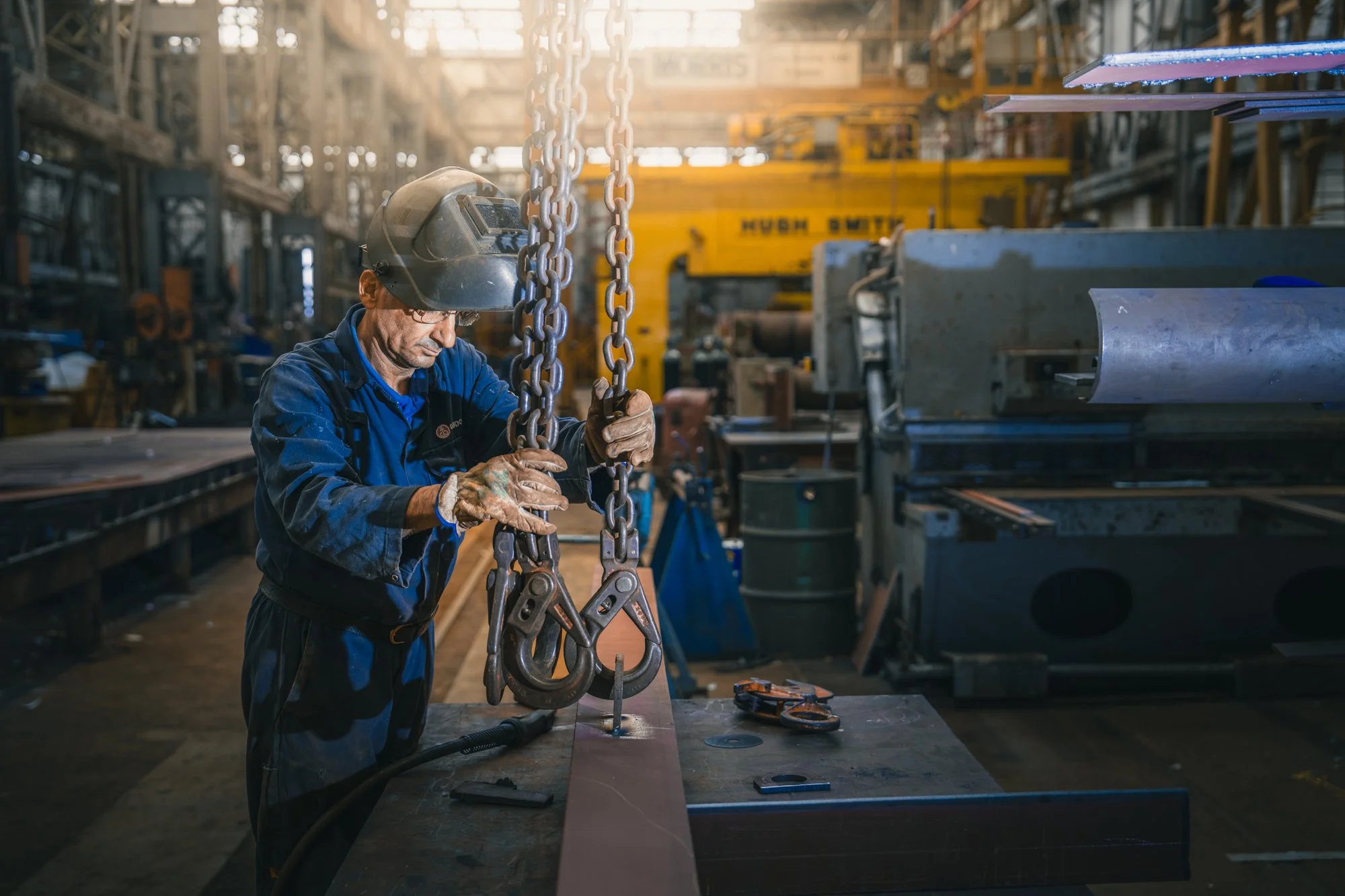 A worker in safety gear, including a helmet and gloves, is inside an industrial factory assembling or inspecting a large metal component surrounded by equipment and machinery.