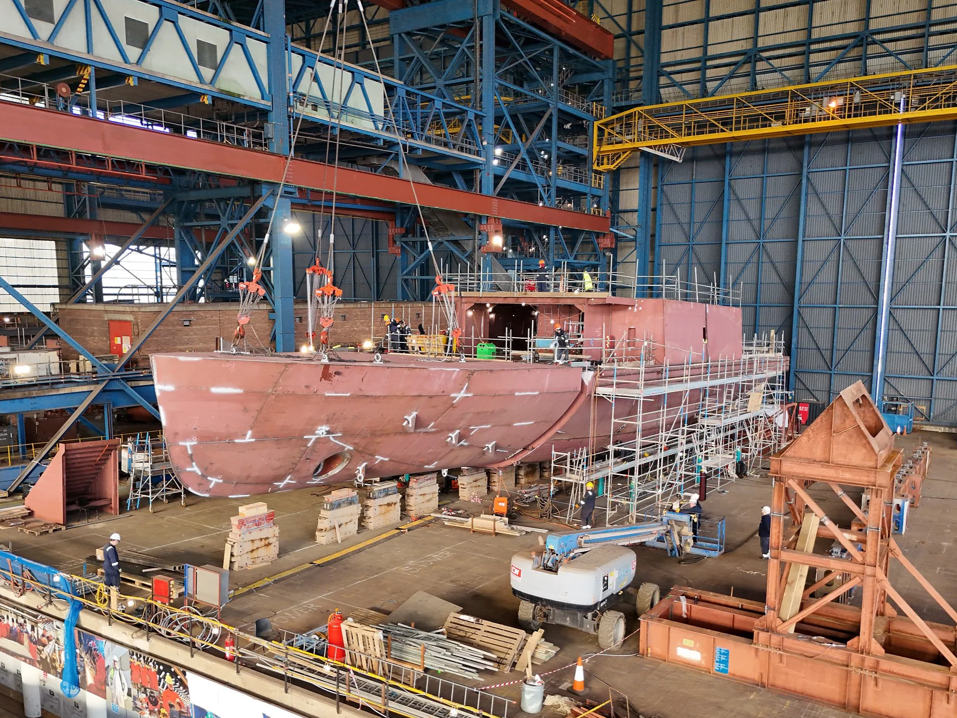 Inside a large industrial shipbuilding factory within Balaena Birkenhead with workers and scaffolding constructing a ship's hull.