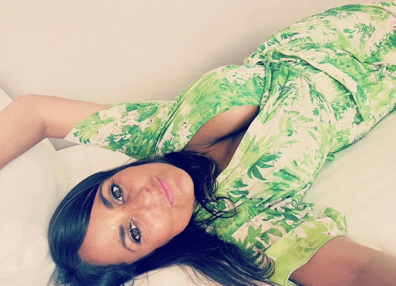 A woman lying on her side on a white bed, wearing a green and white floral robe.