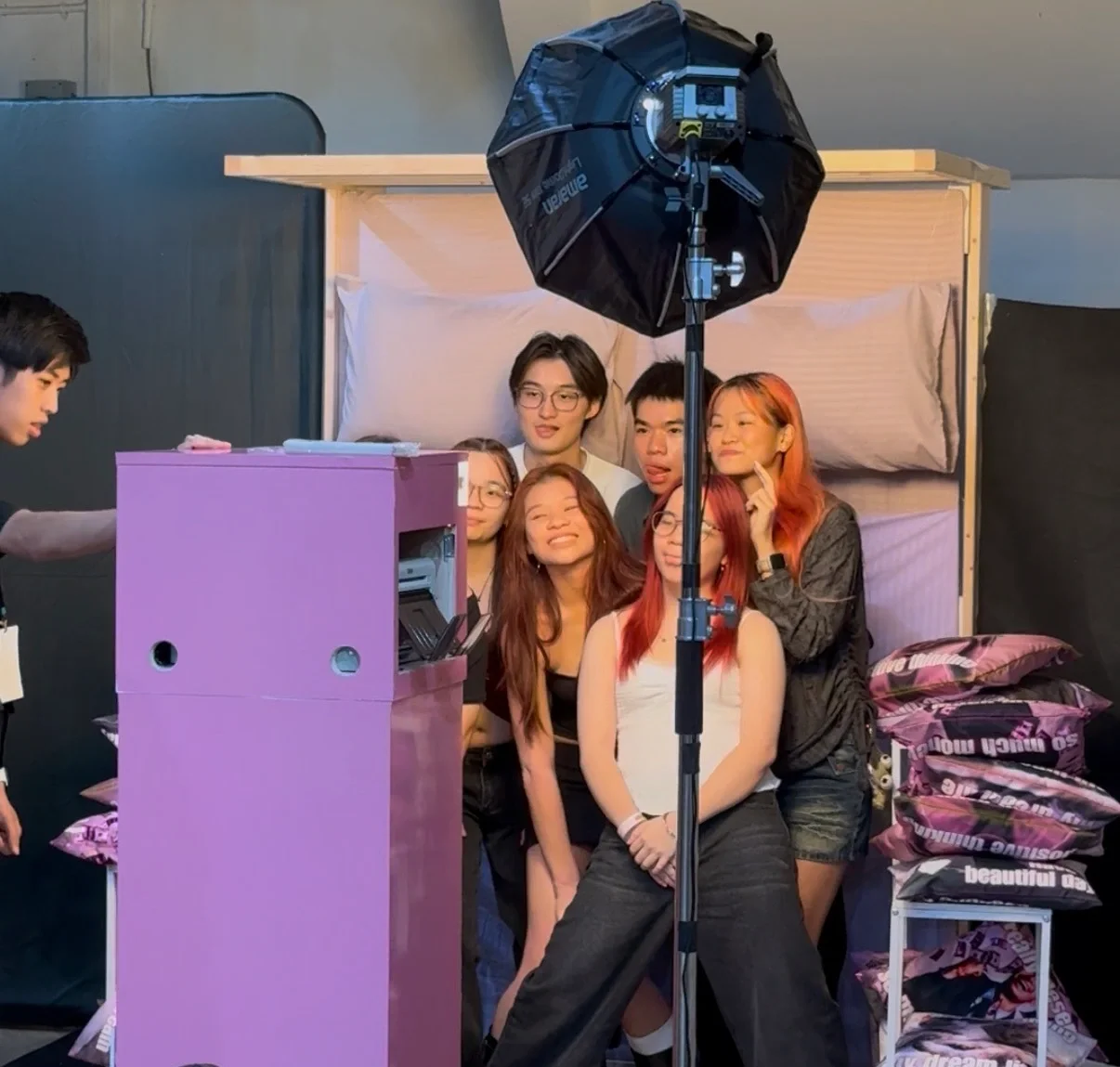 Group of young people taking a photo in a photo booth setup with a backdrop, lighting equipment, and various supplies.