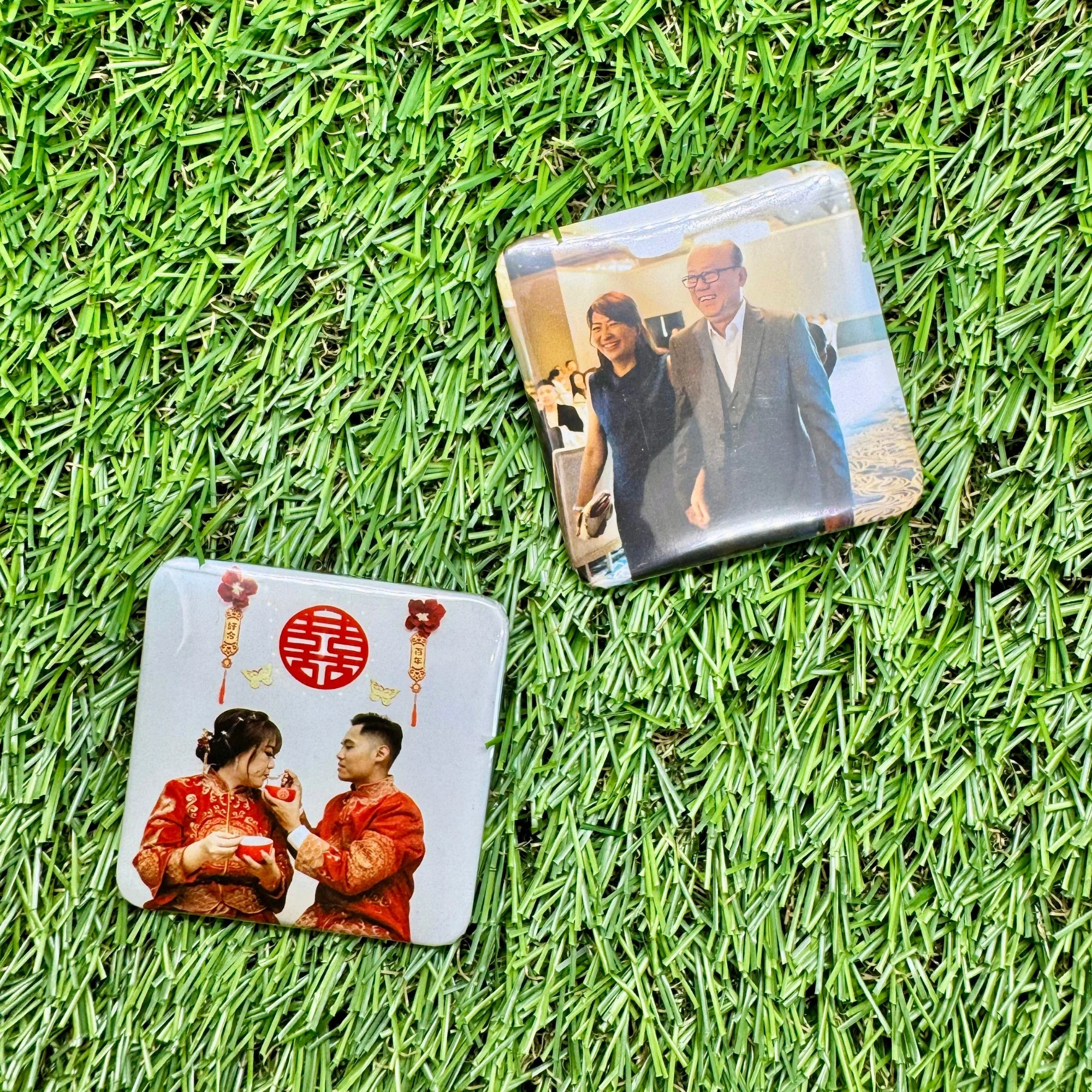 Two square photo tiles placed on a green grass surface. The top photo shows a smiling woman and man walking together at an indoor event. The bottom photo shows a couple in traditional Chinese clothing sharing a moment at a celebration with red and gold decorations.