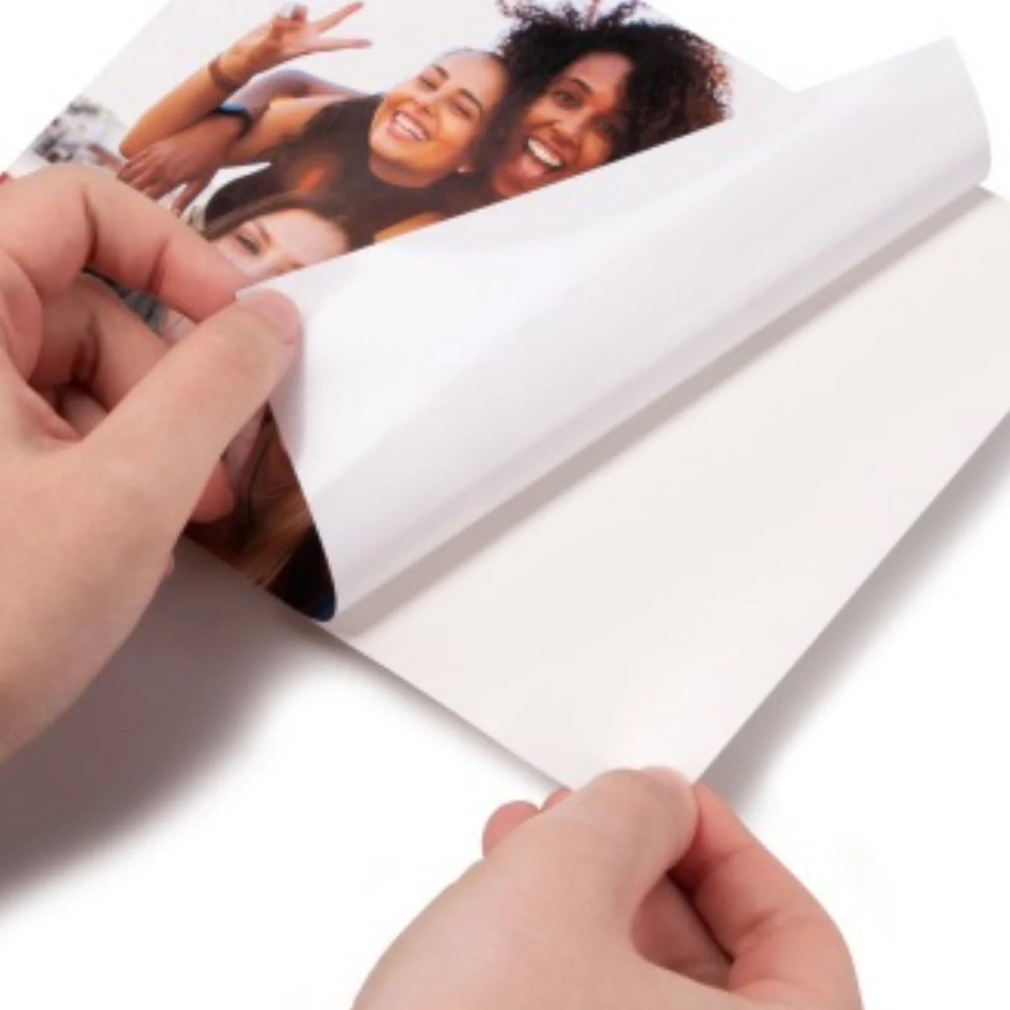 A person is peeling back a photograph of three smiling women, two with curly hair and one with straight hair, on a white surface.