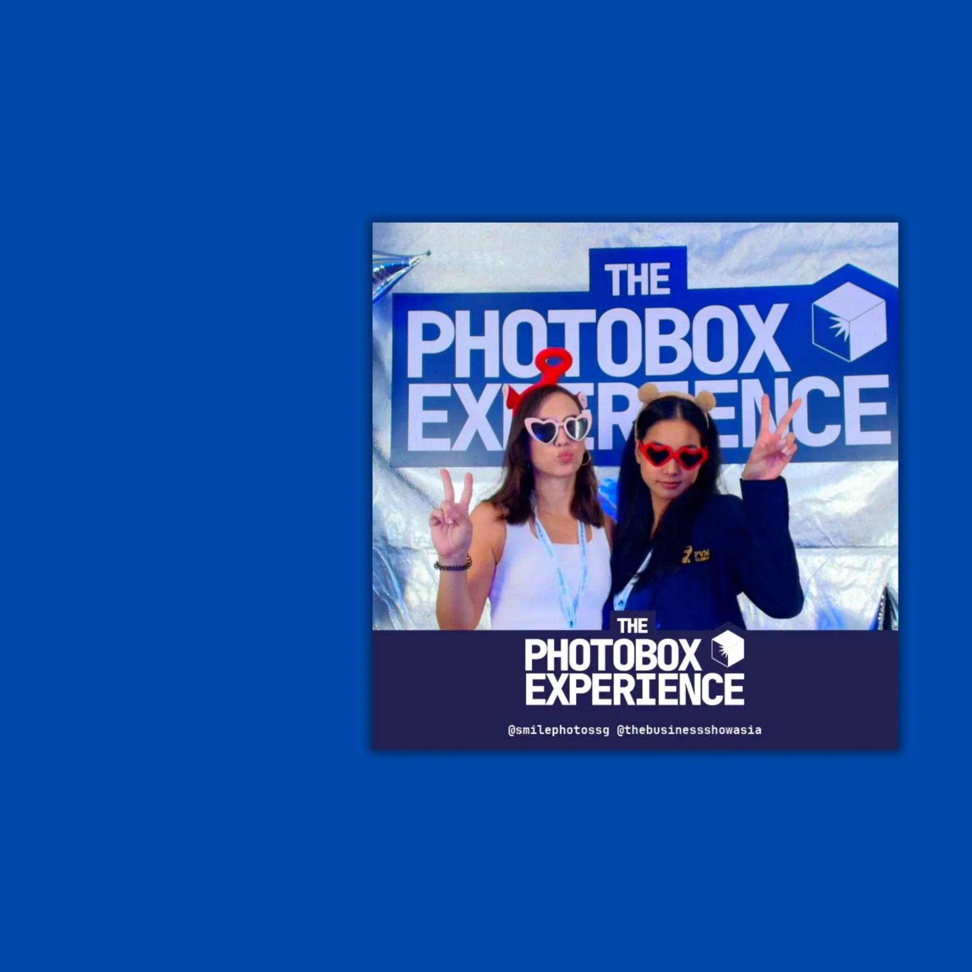 Two women wearing fun sunglasses and headbands posing at the Photobox Experience event.