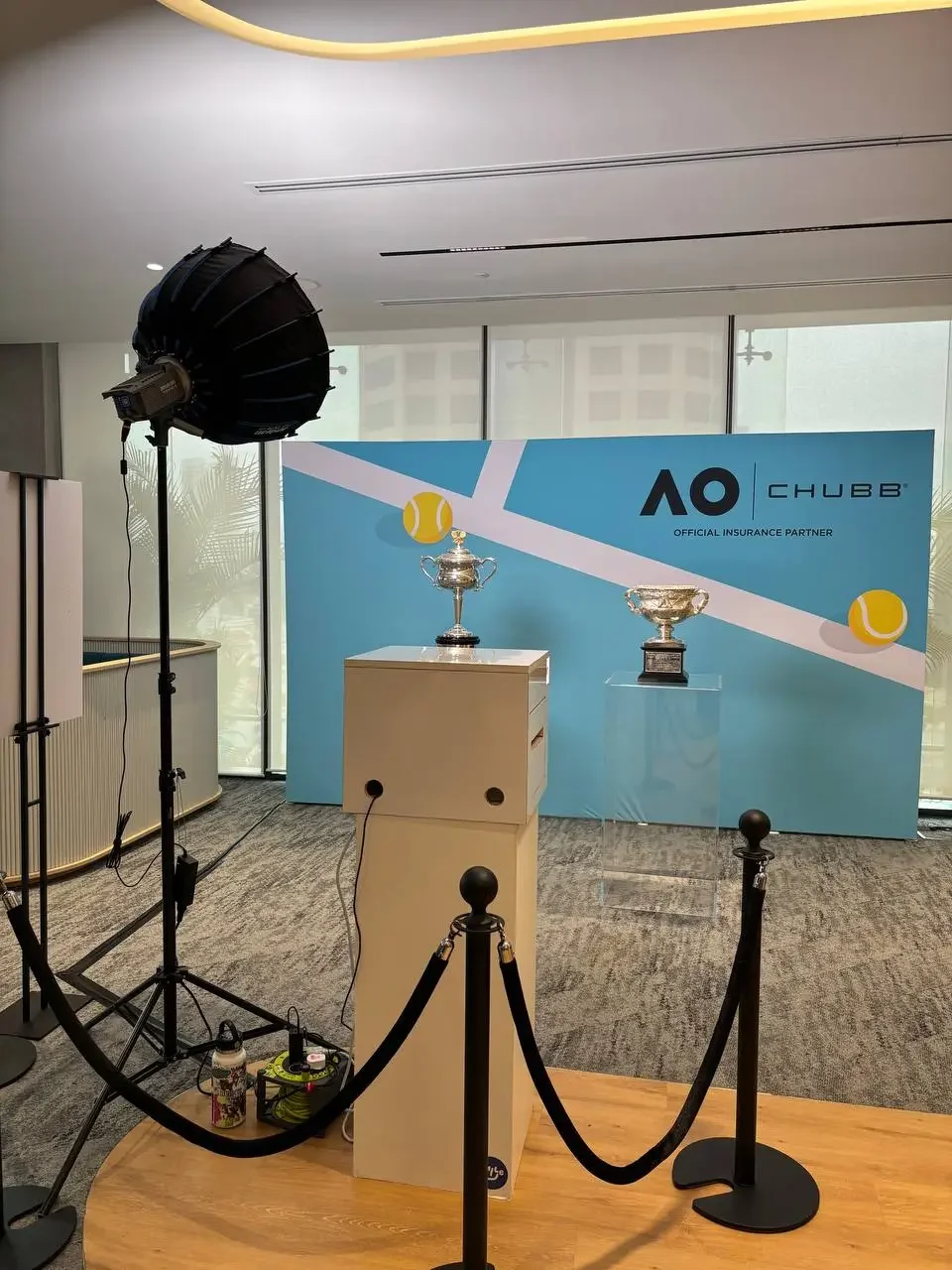 Trophies displayed on pedestals in front of a blue backdrop with AO and CHUBB logos and tennis ball graphics, set up for an award presentation or photo opportunity.