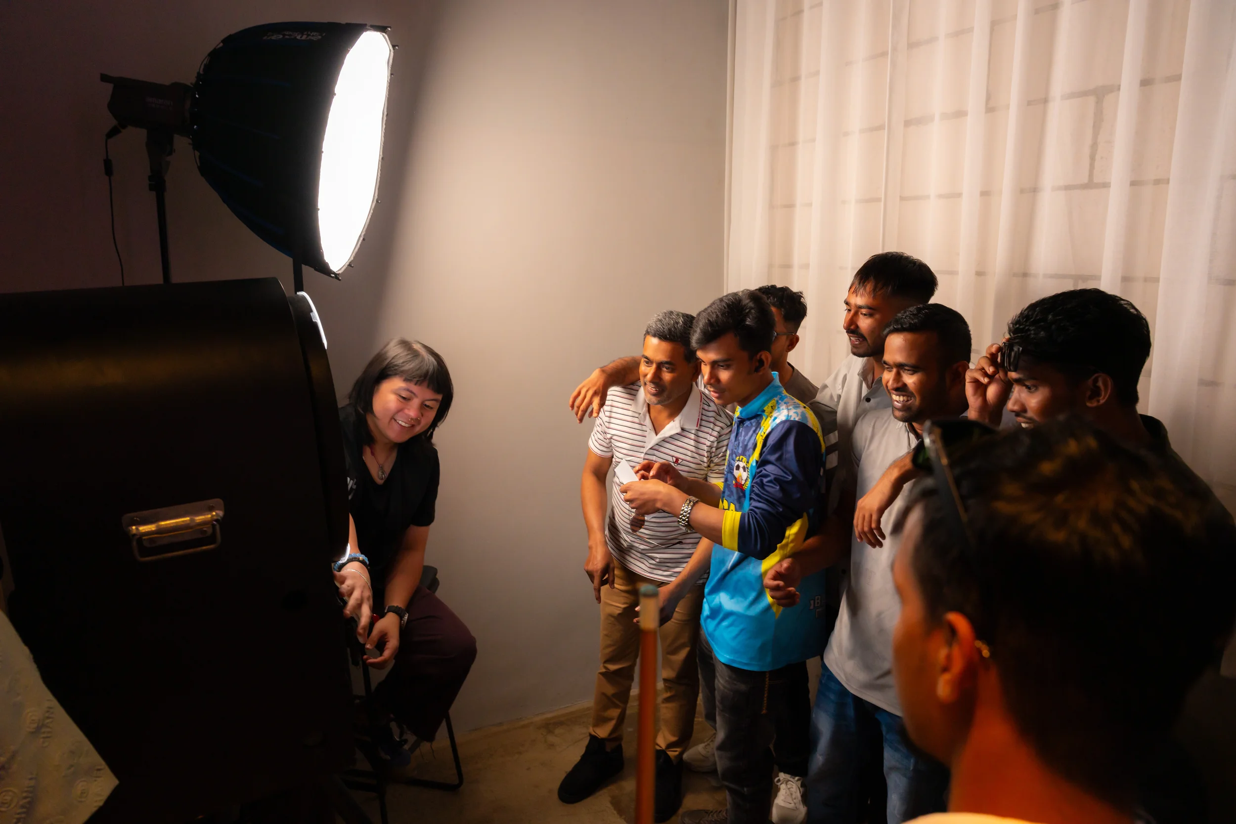 Group of people smiling and posing for a photo in a photography studio with a large softbox light.
