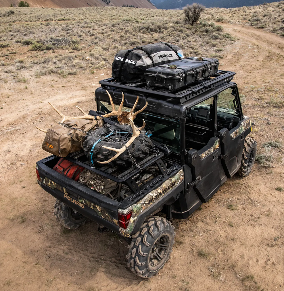 Polaris Ranger med camouflagemönster, laddat med hårda och mjuka väskor på taket samt ett par horn på fronten, i ett ökenlandskap.