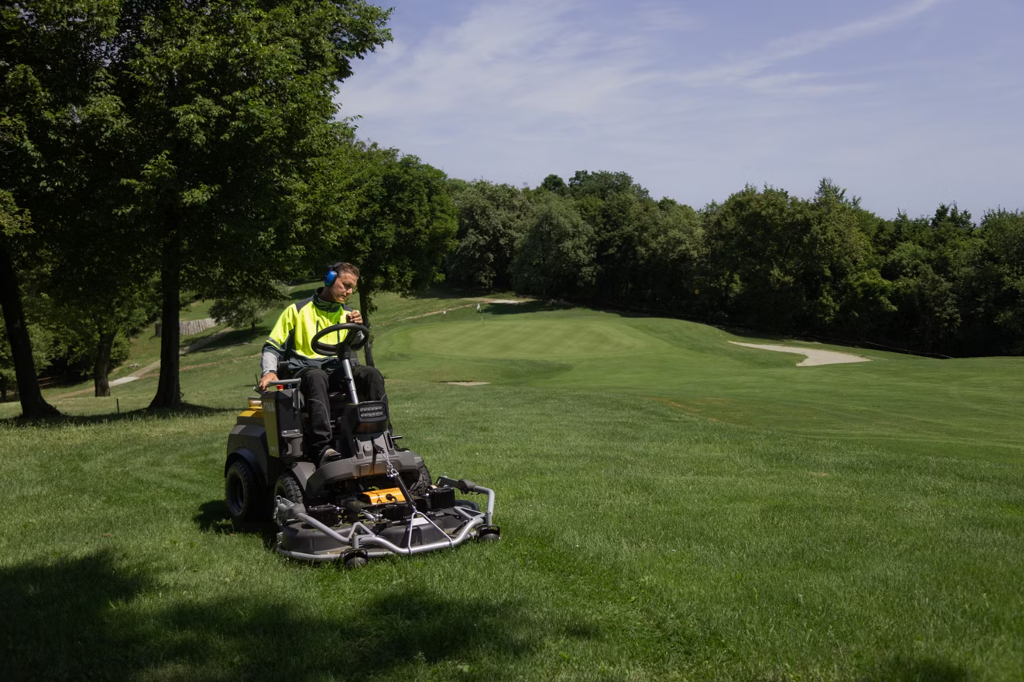 Person som använder en Stiga Park på en golfbana, omgiven av gröna träd och fairways.