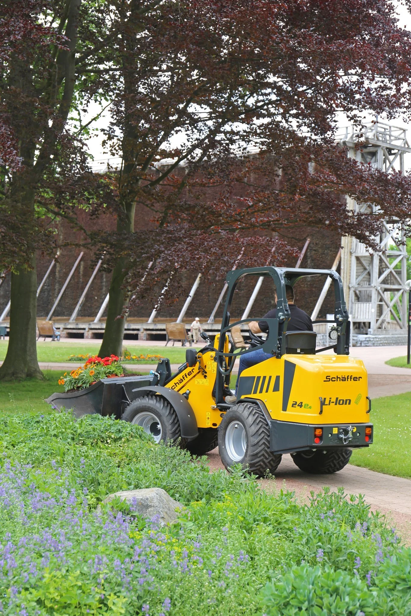 En Schäffer kör på en gräsbana i en park med träd och blommor, och det finns några personer i bakgrunden.