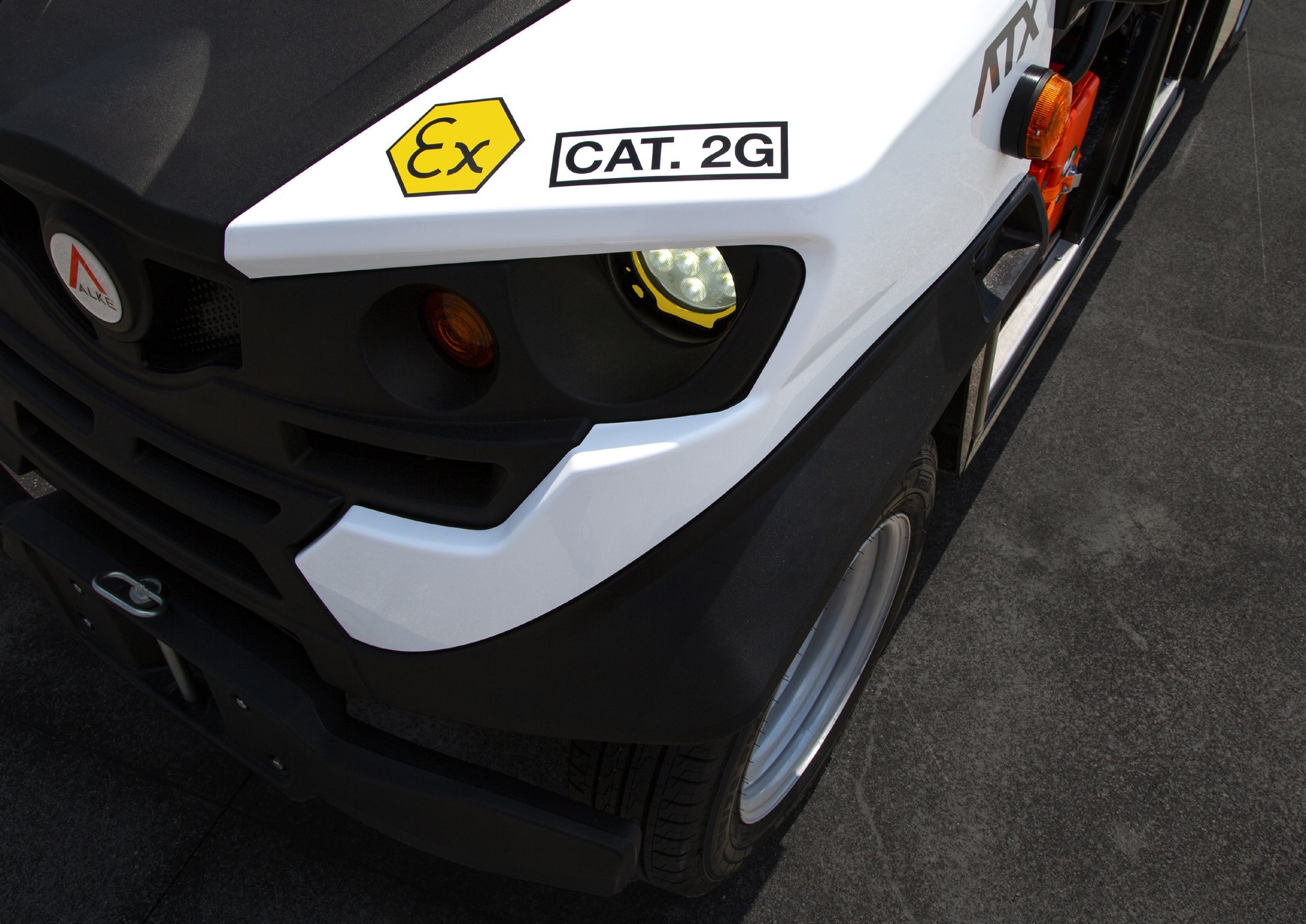 Framsidan av en vit och svart ATEX Alkè  med varningsetiketter, inklusive 'Ex' och 'Cat. 2G', samt ett orange varningsljus och en huvudstrålkastare.