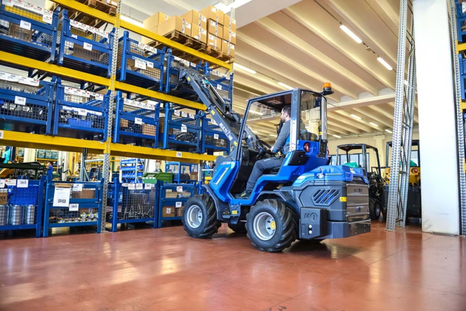 En man kör en liten MultiOne inomhus i ett lager med hyllor fyllda med lådor och förvaringskorgar.