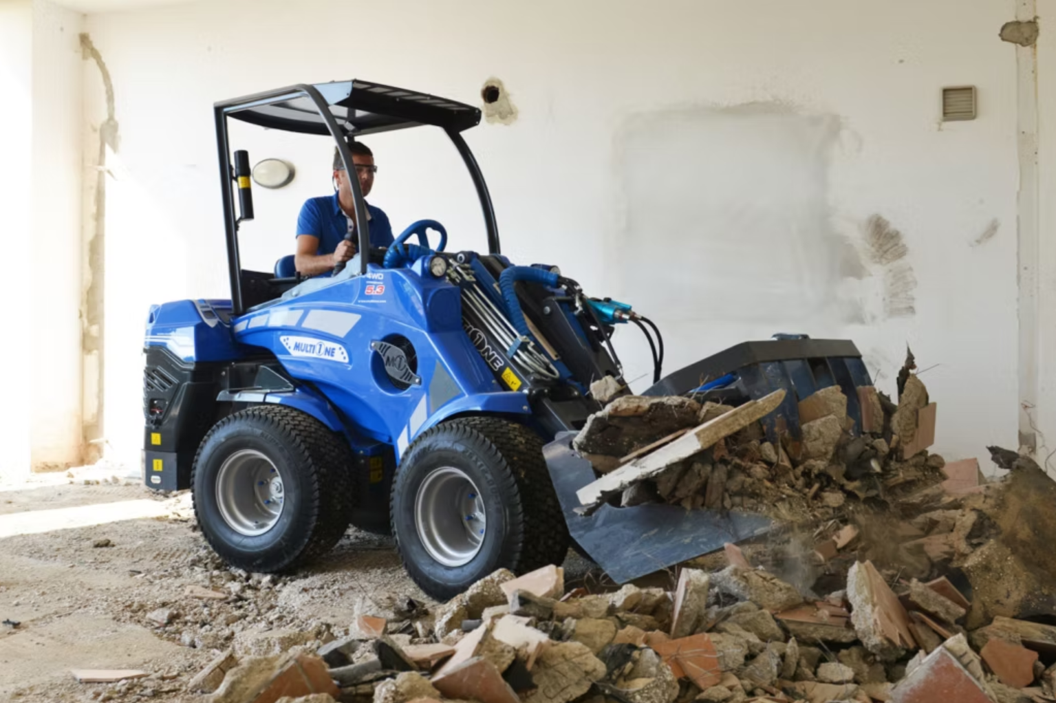 En man kör en MultiOne  inomhus, som används för rivning, och river väggar och golv.
